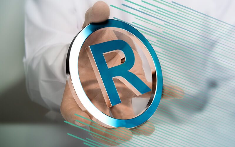 En hånd som holder en R inne i en sirkel av metall, symbolet for registertvaremerke 