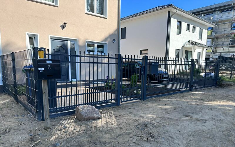 Moderner Doppelstabmattenzaun in Anthrazitgrau mit Tor und Briefkasten, installiert vor einem Neubau mit hellem Putz, das Grundstück ist noch unbepflanzt.