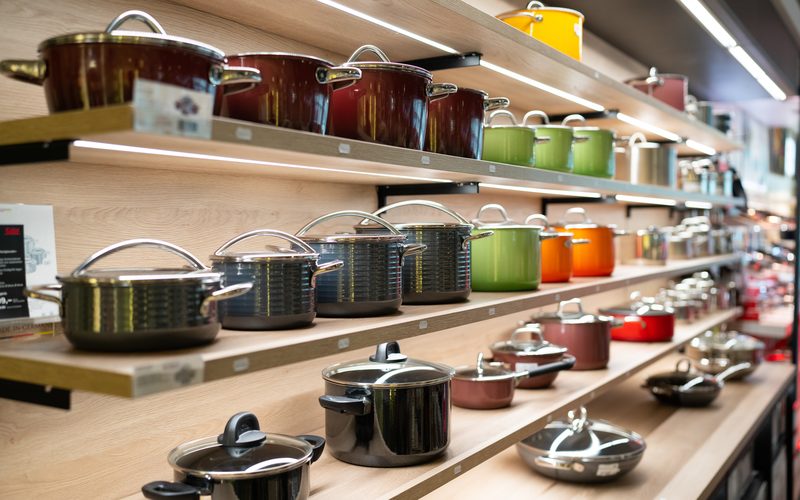 Farbige Kochtöpfe aus Metall auf Holzregalen in einem Geschäft