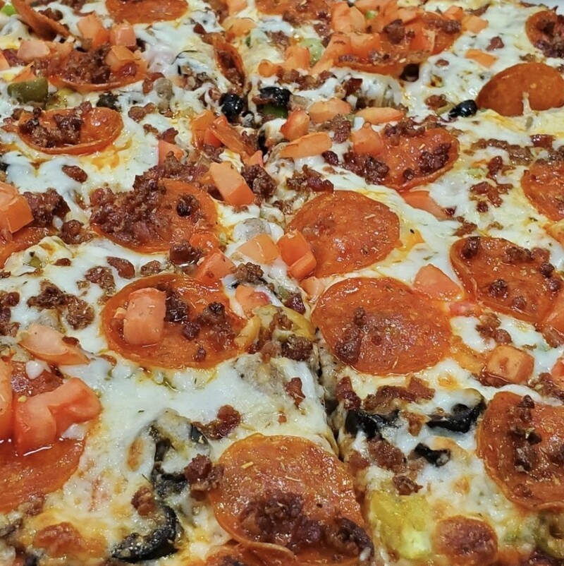 A close-up Pizza "Your Way" with pepperoni, black olives, tomatoes, and bacon bits on a thin crust.