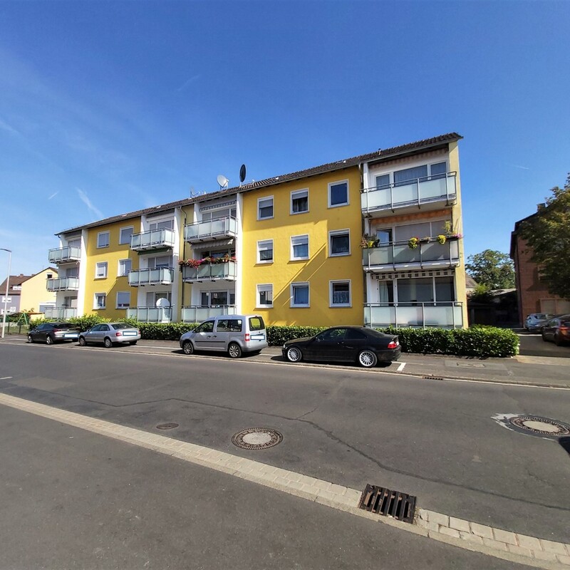 Mehrfamilienhaus mit gelber Fassade, Balkonen und angrenzender Straße