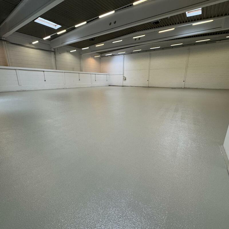 Große, leere Industriehalle mit strapazierfähigem, hellgrauem Epoxidharzboden, weißen Wänden und moderner LED-Deckenbeleuchtung.