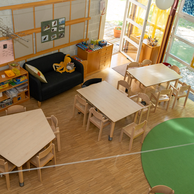 Gruppenraum im Kindergarten – Heller Raum mit Kindertischen, Stühlen und Spiel- sowie Bastelmaterialien