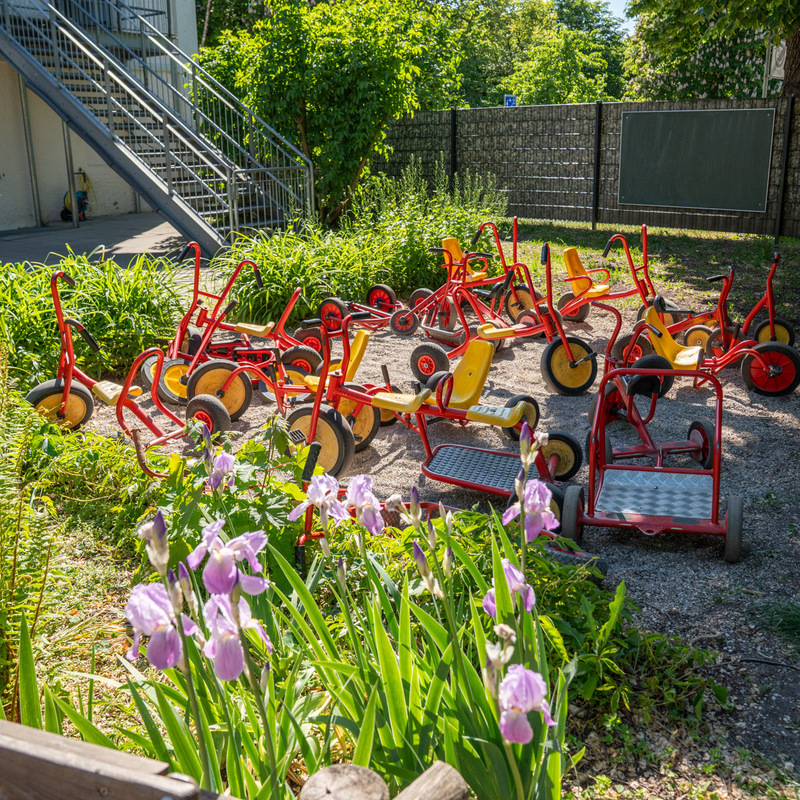Abstellbereich mit roten Kinderfahrzeugen im Garten