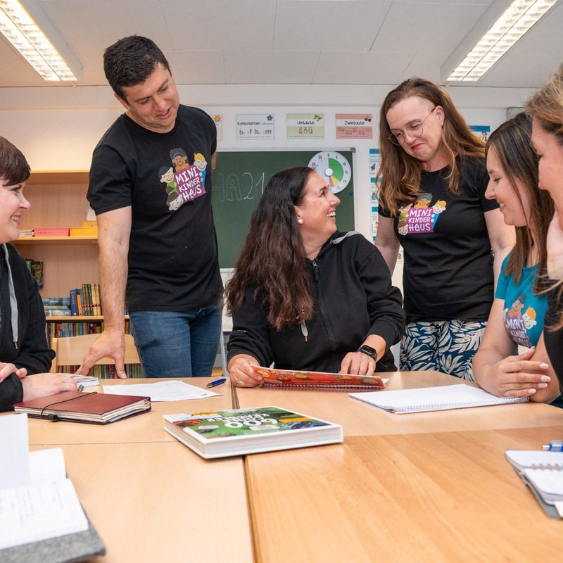 Team des Minikinderhauses sitzt lachend um einen Tisch und bespricht Unterlagen