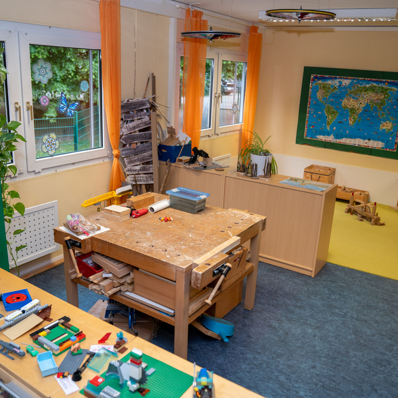 Werkraum mit Arbeitstisch, LEGO-Modellen und Weltkarte an der Wand