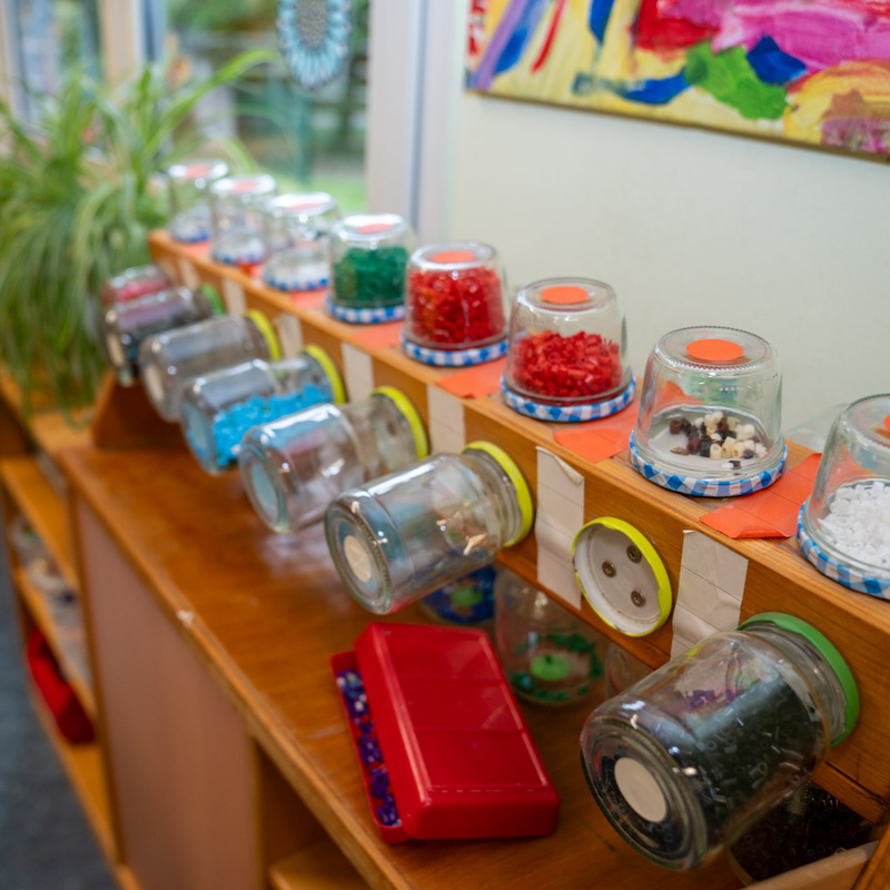 Wandregal mit auf dem Kopf stehenden Gläsern, gefüllt mit bunten Bastelmaterialien