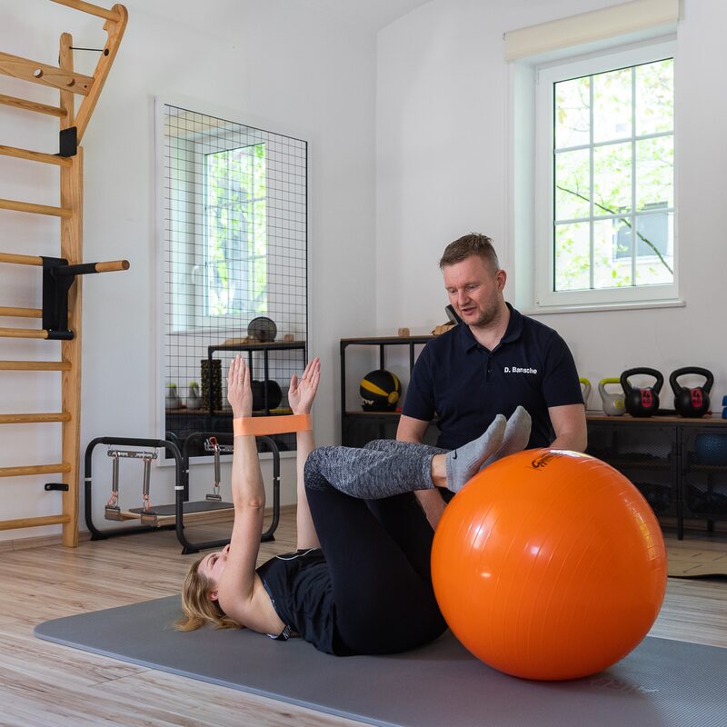 Physiotherapeutin führt Übung mit Patientin am Pezziball durch