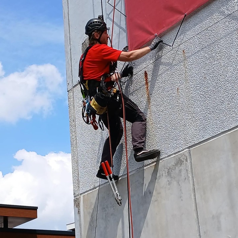 Kletterer befestigt rote Plane an Wand