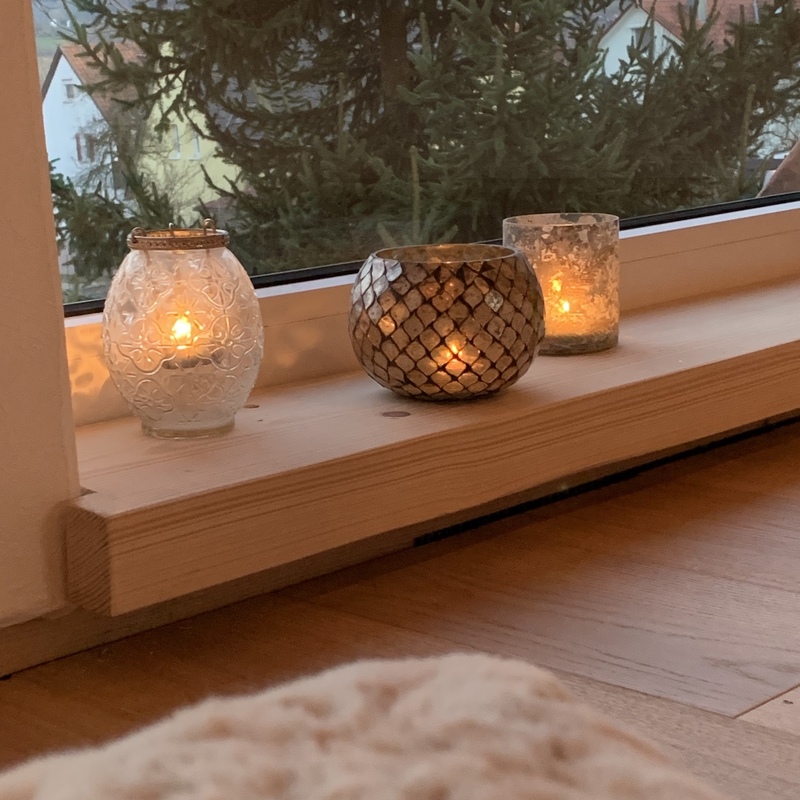 Kleine Windlichter mit Kerzenlicht auf einem Fenstersims mit Blick ins Grüne