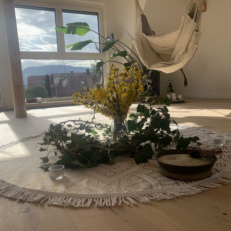 Runde Bastmatte mit Blumen und Klangschale vor bodentiefem Fenster