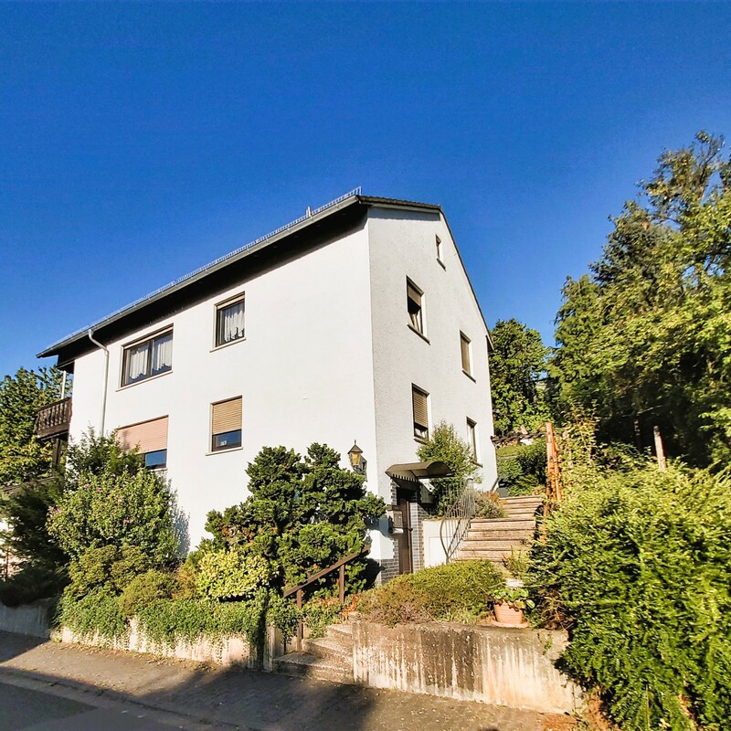 Mehrfamilienhaus in Hanglage mit Treppe, Vorgarten und weißer Fassade