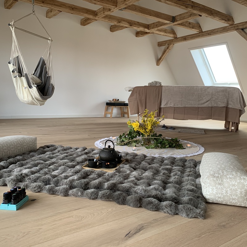 Meditationsbereich mit grauer Matratze, Sitzkissen und Blumen im Tageslicht eines Dachzimmers