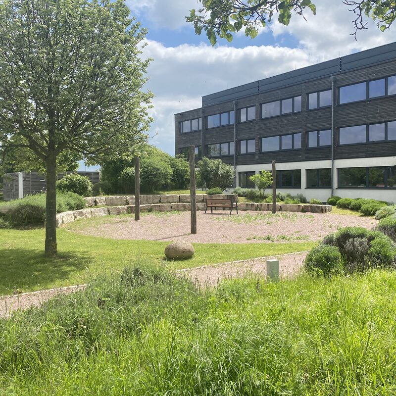 Grüner Außenbereich mit Sitzbank und Bürogebäude