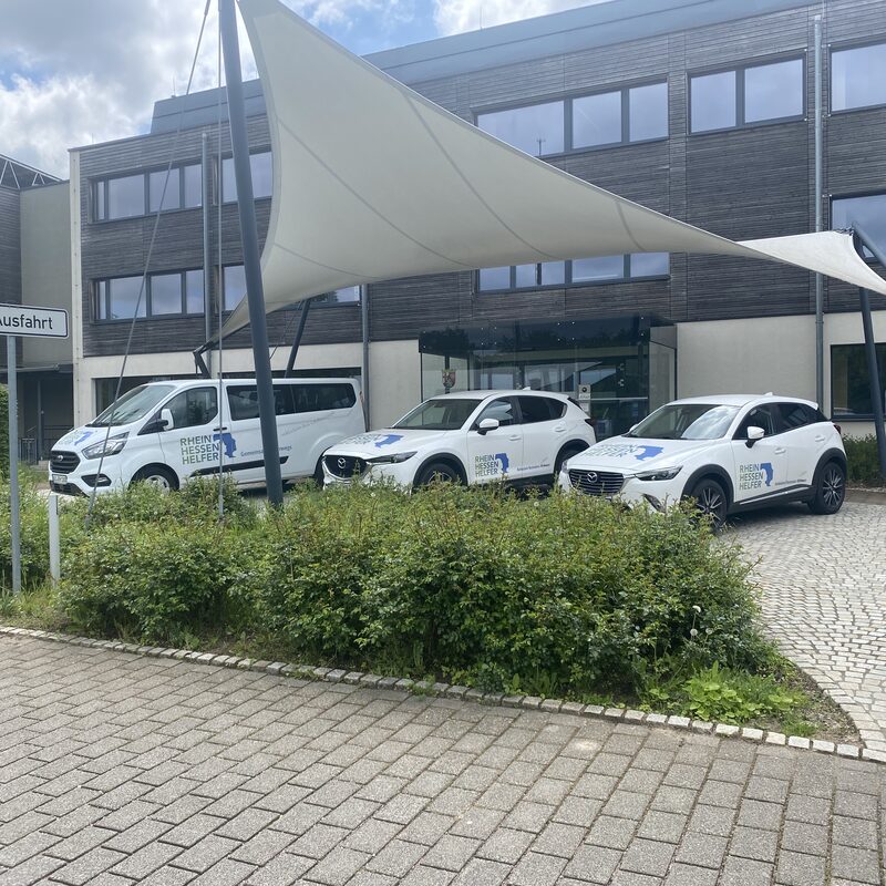 Drei beschriftete Firmenautos vor Gebäude mit Ausfahrt-Schild
