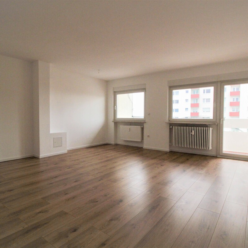 Helles Wohnzimmer mit Holzfußboden, großen Fenstern und Zugang zum Balkon