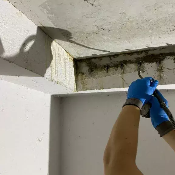 Ein Bauarbeiter führt Abdichtungsarbeiten an einer feuchten Wand durch.