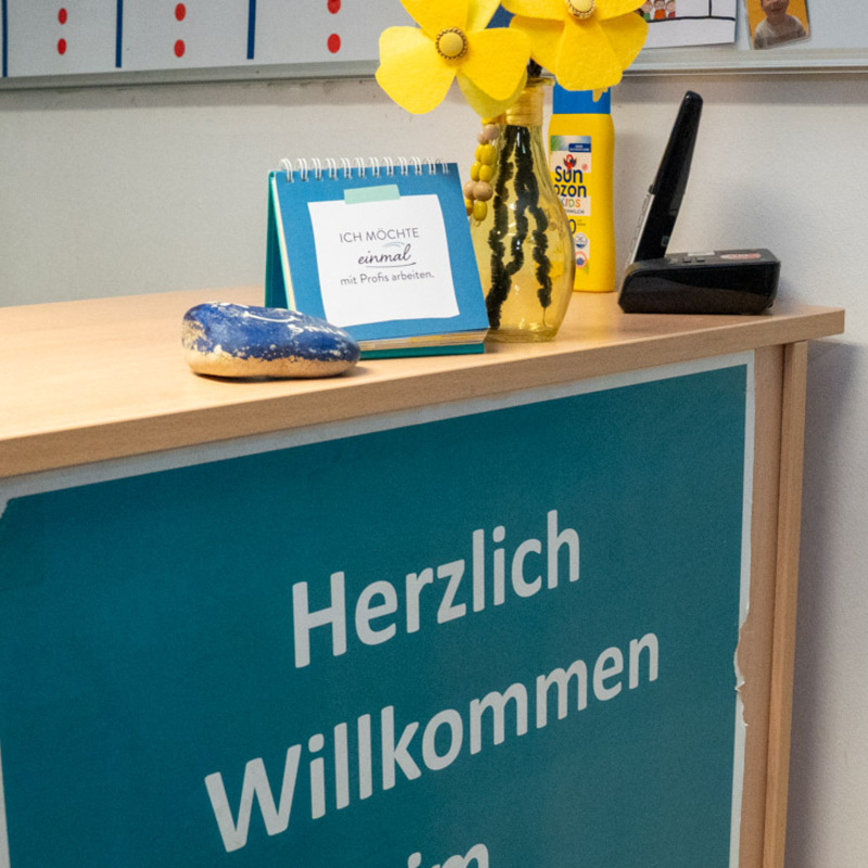 Empfangstresen mit „Herzlich Willkommen“-Schild, Blumen, Sonnenschutzmittel und Fundstücke-Hinweis an der Wand