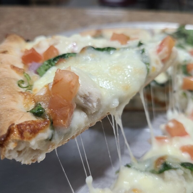 A close-up view of our chicken alfredo pie with onion and spinach added on traditional crust.