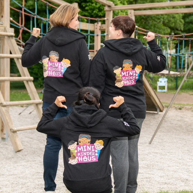 Drei Personen im Minikinderhaus-Hoodie zeigen das Logo auf dem Rücken