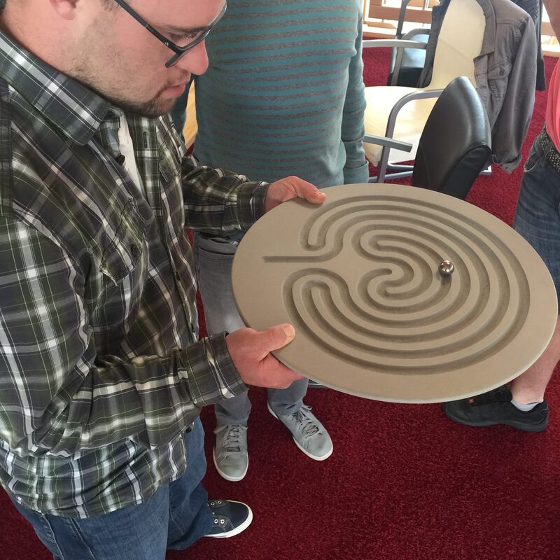 Mann hält rundes Labyrinthspiel mit Metallkugel in der Hand