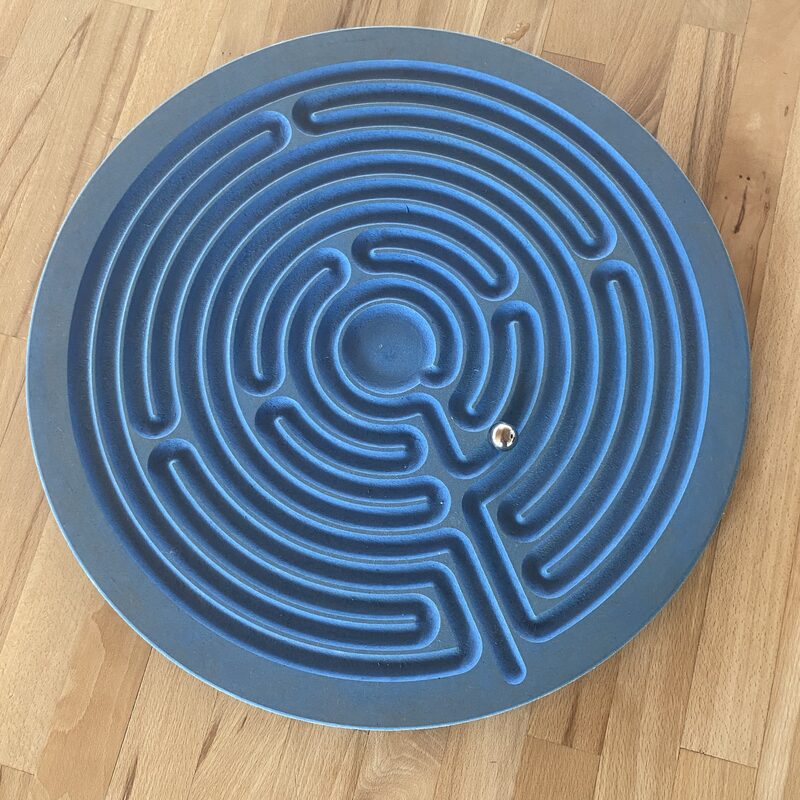 Rundes, blaues Labyrinth mit Metallkugel auf Holztisch