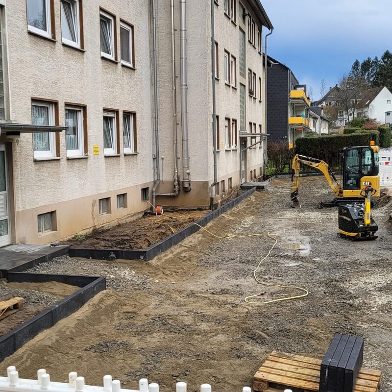 Baufläche mit Bagger an mehrstöckigem Wohnhaus