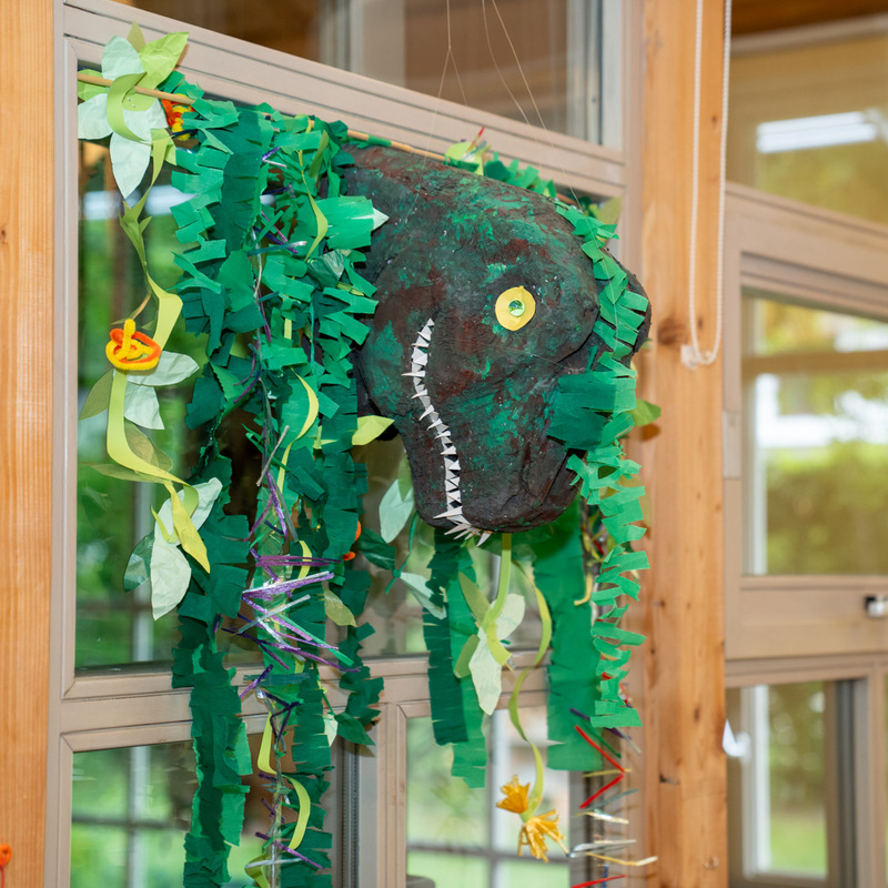 Gebastelter Dinosaurierkopf mit grünen Papierblättern als Dekoration