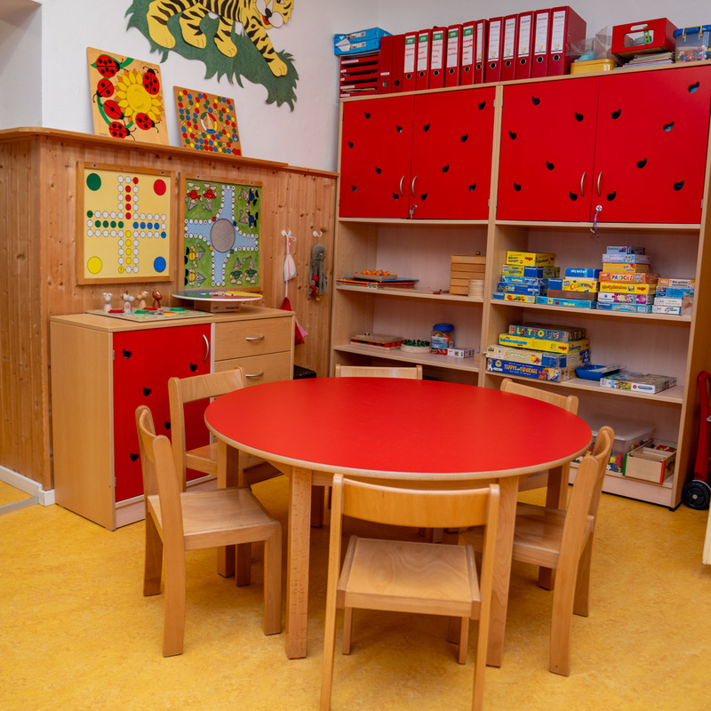 Spiel- und Bastelraum mit rotem Rundtisch und Spiele-Regalen