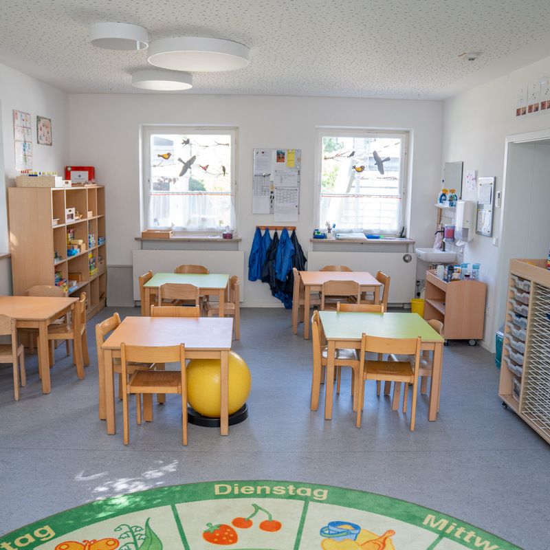 Gruppenraum mit Tischen, Stühlen und Spiele-Regalen