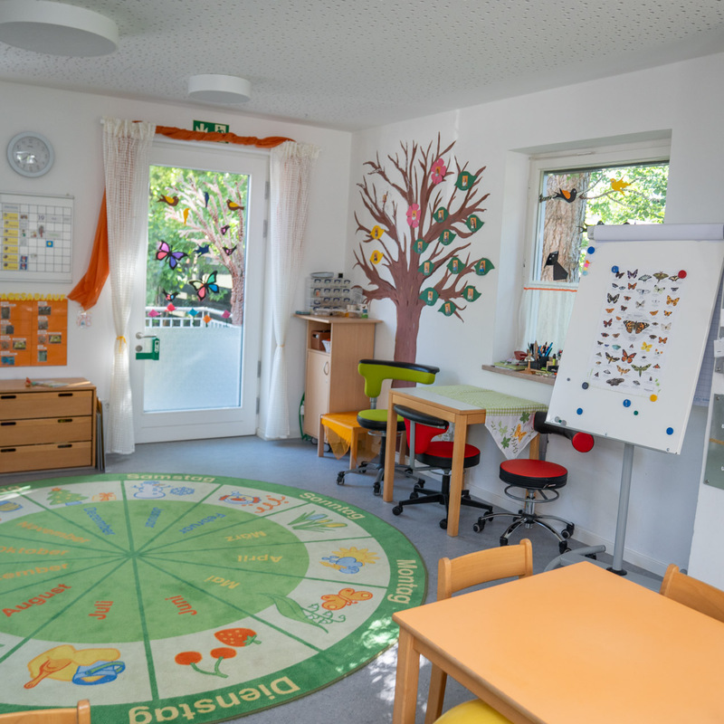 Gruppenraum mit Spielteppich, Tischen und Wanddekorationen