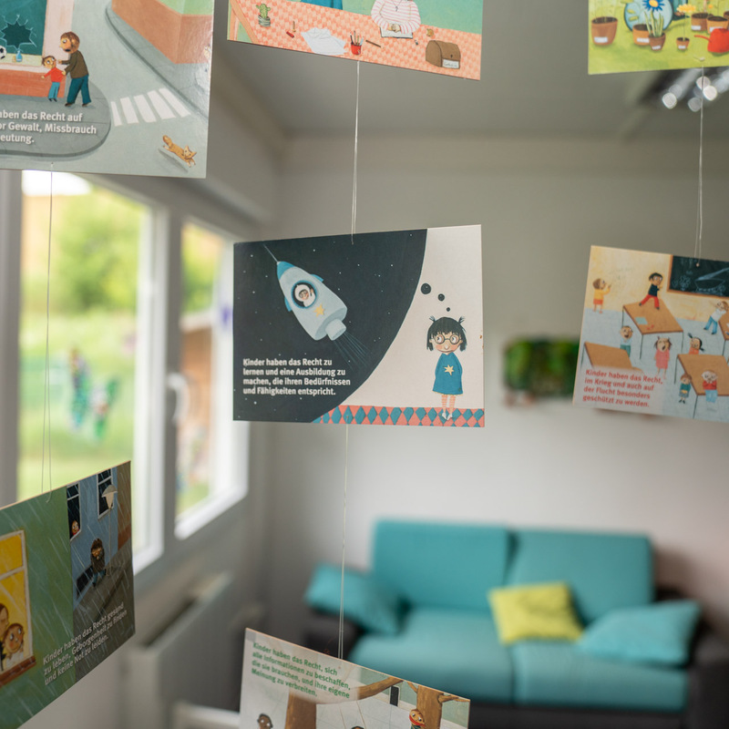 Hängende Karten mit Kinderrechten, illustriert und beschriftet, vor einem Sofa
