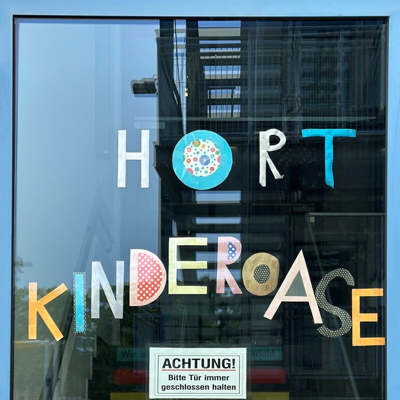 Glastür mit der Aufschrift „Hort Kinderoase“ und Hinweisschildern
