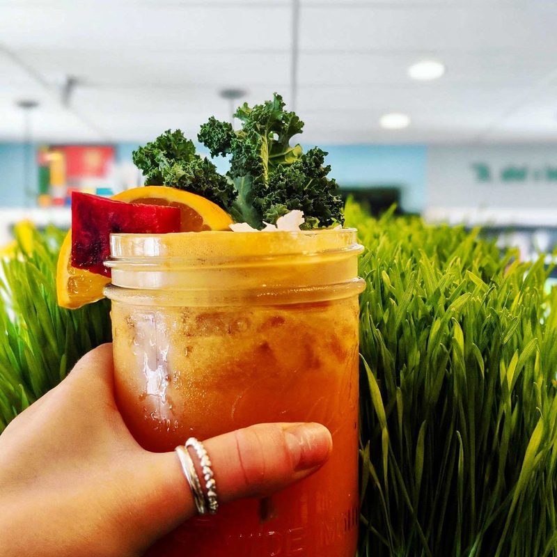 Fresh orange colored juice in front of a grass background. The juice has kale, watermelon and orange garnish.