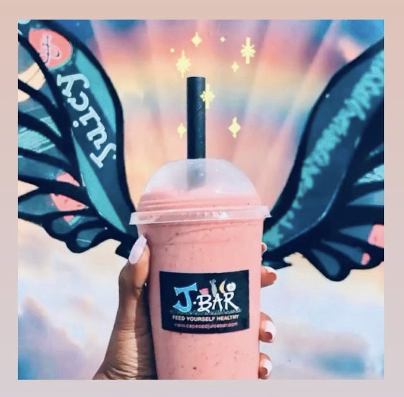 A pink J Bar smoothie is held up in front of an inspirational mural