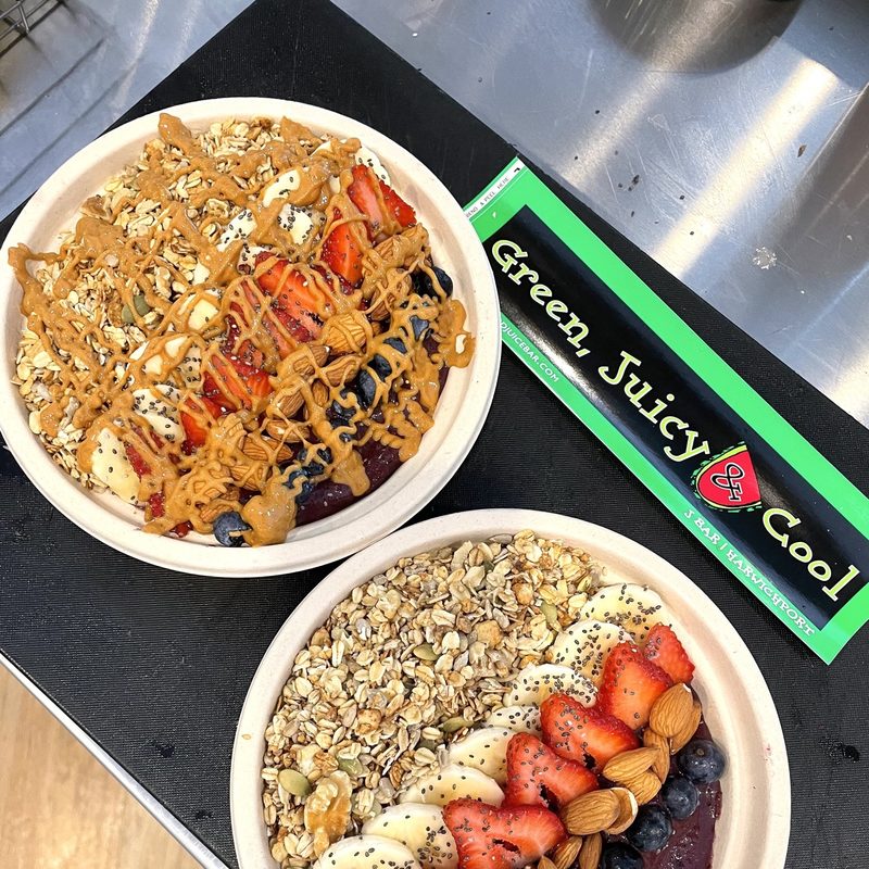 Two breakfast bowls include oatmeal, almonds, bananas, blueberries, strawberries and a peanut butter drizzle