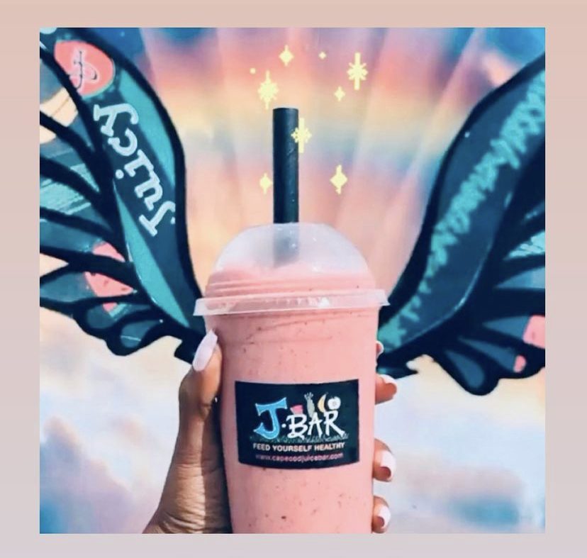 A pink J Bar smoothie is held up in front of an inspirational mural