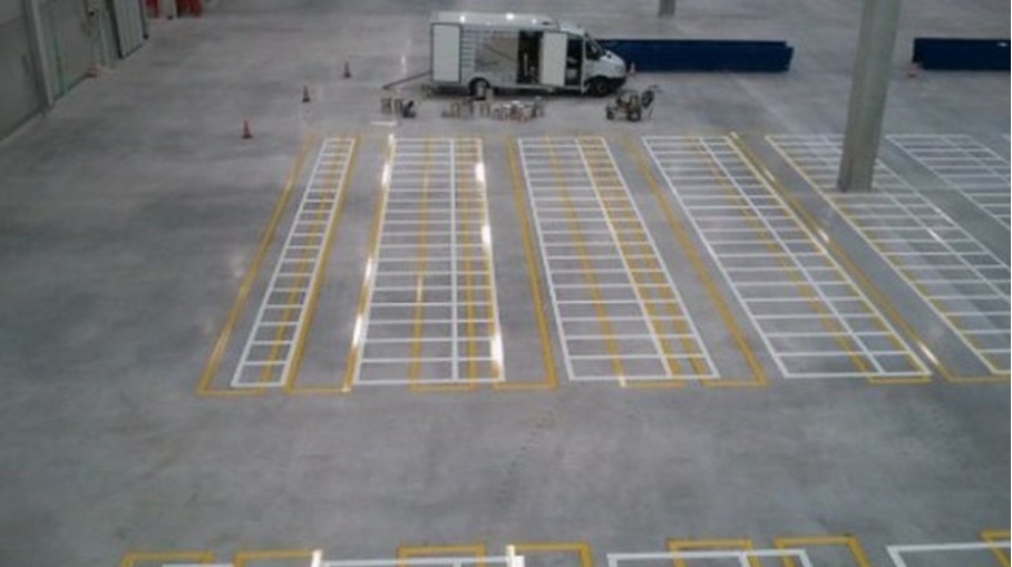 Innenbereich einer Industriehalle mit frisch aufgebrachten weißen und gelben Markierungen für Palettenfelder und Lagerflächen.