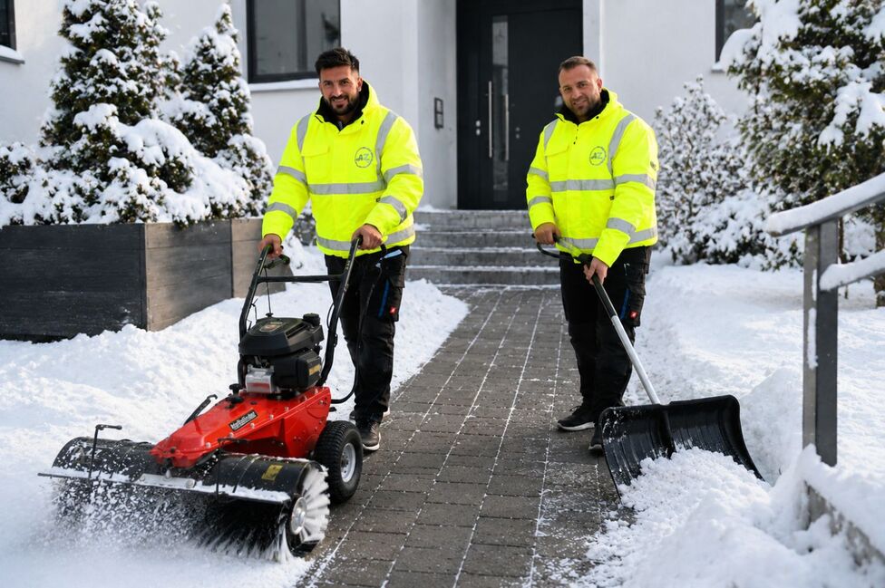 Zwei Mitarbeiter von AZ-Clean räumen mit Kehrmaschine und Schneeschieber den Zugang zu einem Wohnhaus